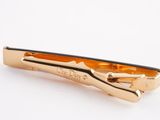a gold tie bar that is on a white surface