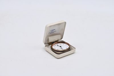 une petite montre de poche posée sur une surface blanche