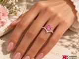 woman ' s hand with pink manicured nails holding a pink diamond ring