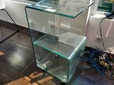 une table en verre surmontée d'une étagère en verre, placée devant une fenêtre