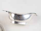 a silver sauce boat and a silver spoon on a white table