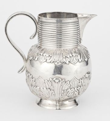 an antique silver pitcher with a handle and a flower design