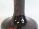 a black vase with red paint on it on a white background