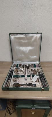 silverware in a green case on a wooden table next to a white wall