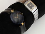 une montre noire posée sur une serviette noire, avec un bracelet doré