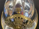 un casque de pompier argenté et doré posé sur une table noire