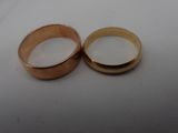 two gold wedding rings on a white surface