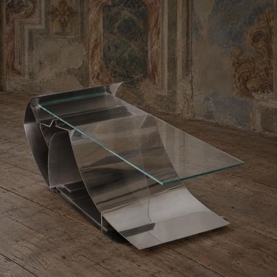 une table en verre avec un plateau incurvé, posée sur un parquet