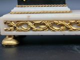 a white and gold clock on a stand on a table