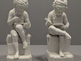 une paire de statues blanches représentant des enfants assis sur des tabourets en train de lire un livre