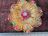 un gros plan d'une broche en or sertie de pierres roses et vertes