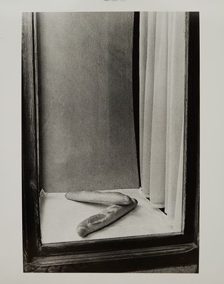photographie en noir et blanc d'une miche de pain posée sur une table devant une fenêtre