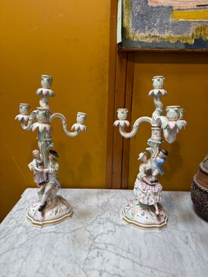 two candles that are sitting on a table in front of a painting