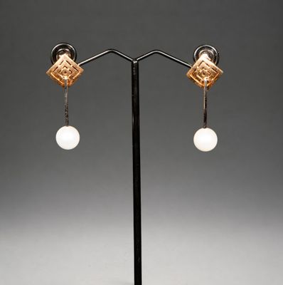 une paire de boucles d'oreilles en or et perles posée sur un socle noir
