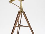 un télescope en laiton posé sur un trépied en bois, devant un fond blanc