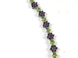 Collier de perles violettes et vertes sur fond blanc, avec un fermoir en argent