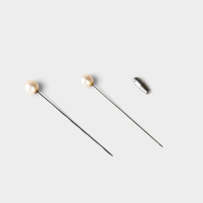 three pairs of pins with pearls on them on a white surface