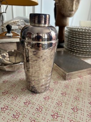 un shaker à cocktail argenté posé sur une table, à côté d'une pile d'assiettes