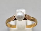 un gros plan d'une bague en or sertie d'une perle blanche