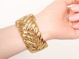 someone is holding a gold bracelet with a braid design on it