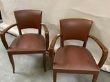 two brown leather chairs sitting next to each other in front of a white wall