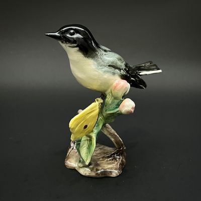 une figurine représentant un oiseau perché sur une branche, entouré de fleurs