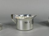 a silver pitcher next to a silver cup on a table