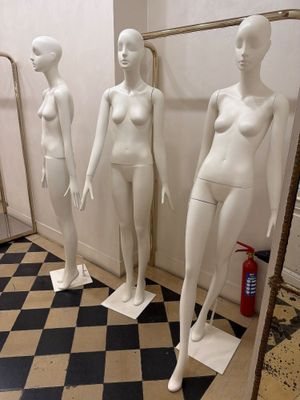 trois mannequins debout dans une pièce dont le sol est en damier noir et blanc
