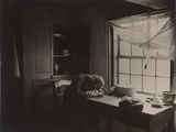 black and white photograph of a cat sitting at a table in front of a window