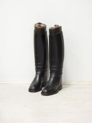 pair of black leather riding boots sitting against a white wall