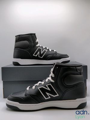 black and white new balance high top sneakers on display in front of a box