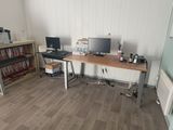 a desk with two computers and a bookcase in the corner