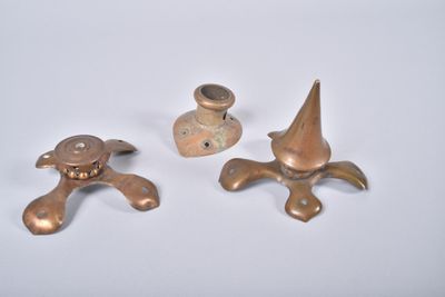 trois pièces métalliques posées sur une surface blanche, avec une lumière en arrière-plan