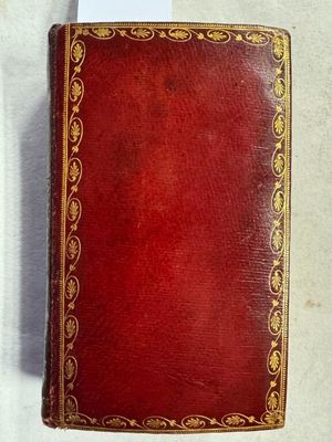 un vieux livre rouge avec des bordures dorées posé sur une surface blanche
