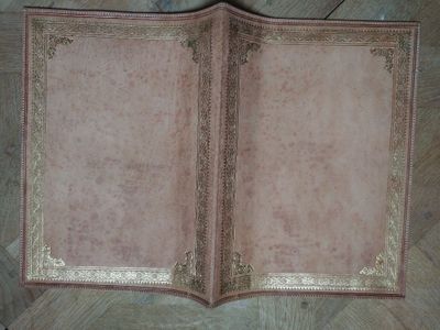 un livre rose aux bords dorés posé sur un parquet