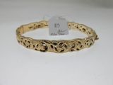 a gold bracelet with filigree design on a white background