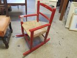 a red rocking chair with a wicker seat in the middle of a room