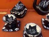cinq théières et tasses en forme de chat, noires et blanches, posées sur la table