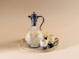 a white and gold pitcher and a cup on a plate