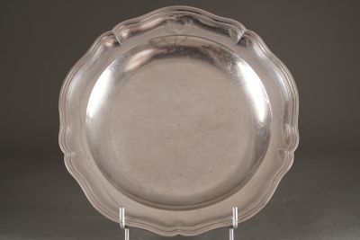 un plat en argent ancien posé sur un support, sur fond gris