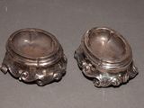 two silver dishes sitting on a table with a black background