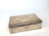 une vieille boîte en argent portant une inscription, posée sur une surface blanche