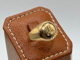 an image of a gold signet ring sitting on top of a brown leather case