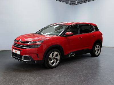 Une voiture rouge est garée dans une pièce blanche au sol noir.