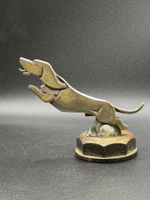 sculpture en bronze représentant un chien sautant par-dessus une balle, posée sur un socle