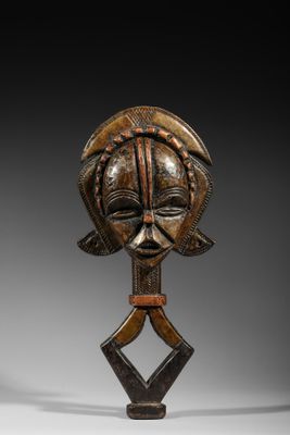 un masque en bois représentant un visage et deux mains, posé sur un socle