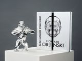 une figurine en argent représentant un robot, posée sur un socle blanc
