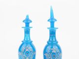 two blue glass bottles with gold designs on them on a white background