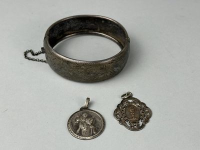 two pieces of silver jewelry on a white surface with a chain around it