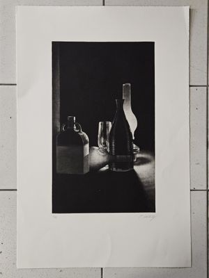 une photo en noir et blanc représentant une bouteille de vin et un verre posés sur une table